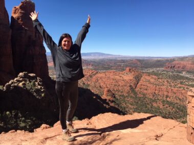 A woman standing on top of a mountain with her arms in the air.