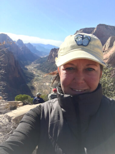 A woman in a hat is standing on top of a mountain.