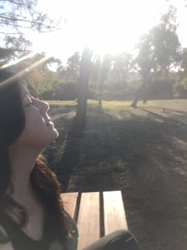 A woman sitting on top of a bench in the sun.