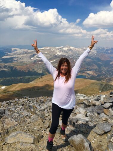 A woman standing on top of a mountain with her hands in the air.