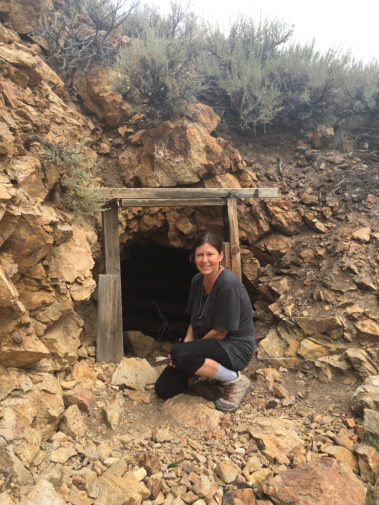 A woman sitting in front of an open cave.