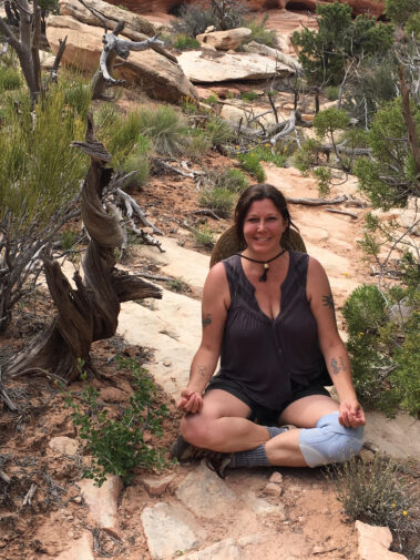 A woman sitting on the ground in front of some trees